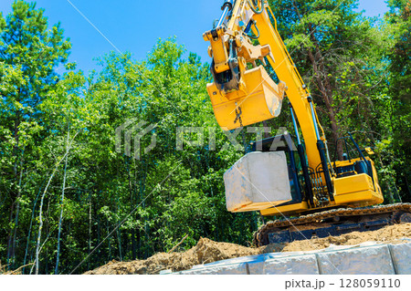 Heavy machinery is actively lifting concrete block at construction site on build retaining walls 128059110