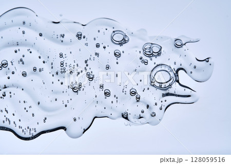 A beautiful drop of cosmetic product with bubbles on a blue background. A beautiful drop of cosmetic product with bubbles on a blue background. 128059516