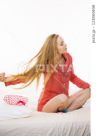 Young woman sitting on bed wearing pajamas Young woman sitting on bed wearing pajamas 128060696