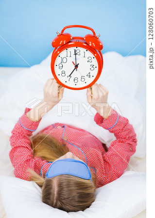 Sleeping woman wearing pajamas holding clock Sleeping woman wearing pajamas holding clock 128060703