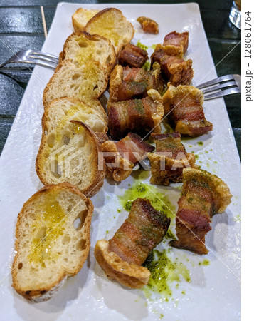 A plate of crispy pork belly and toasted bread with drizzled oil, perfect for sharing. The dish is served on a white plate with a green sauce. 128061764