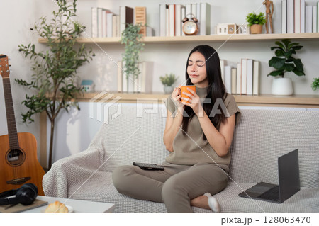 Cozy Home Relaxation. Young woman enjoying a warm drink on a comfortable sofa. Cozy Home Relaxation. Young woman enjoying a warm drink on a comfortable sofa. 128063470