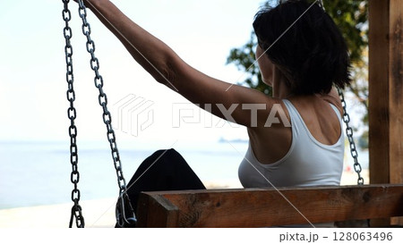 Happy woman ride on swing at tropical at sea beach. Carefree lady enjoying rest near ocean. Adult female having fun at sea shore on sunny day. Concept of summer vacation or holiday. Slow motion Happy woman ride on swing at tropical at sea beach. Carefree lady enjoying rest near ocean. Adult female having fun at sea shore on sunny day. Concept of summer vacation or holiday. Slow motion 128063496