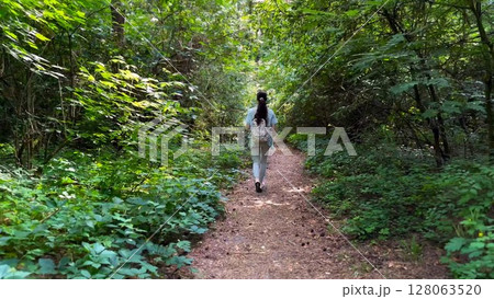 Young woman going along path at summer forest. Female with backpack walking among trail at wild nature. Unrecognizable girl enjoying stroll outdoor admiring beautiful scenic. Close up Rear view 128063520