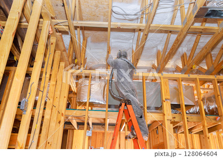 Worker uses spray foam application to insulate ceiling beams in residential construction works Worker uses spray foam application to insulate ceiling beams in residential construction works 128064604
