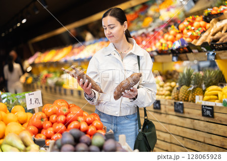 Middle-aged woman choosing cassavas in grocery store 128065928