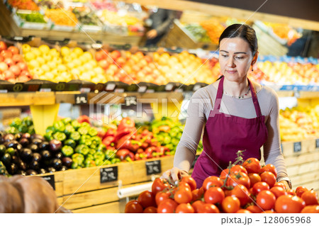 Middle-aged female seller putting tomatoes on counter in grocery market 128065968