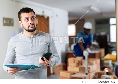 Engineer with documents is talking on a mobile phone Engineer with documents is talking on a mobile phone 128066153
