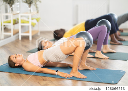 Young woman doing pilates with soft ball in group 128066218
