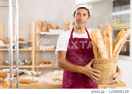 Caucasian male cook-baker worker with basket of baguettes, shows many products 128066239