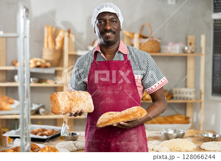 Portrait of experienced baker with tasty hot bread and baguettes in hands in kitchen Portrait of experienced baker with tasty hot bread and baguettes in hands in kitchen 128066244