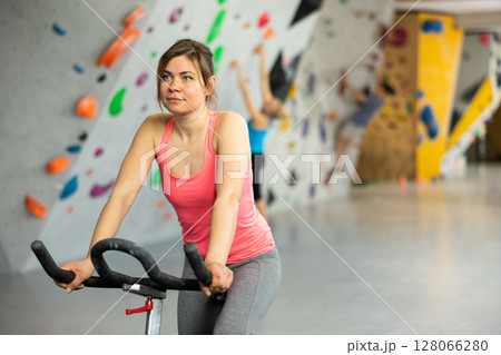 Sports girl on an exercise bike in climbing hall Sports girl on an exercise bike in climbing hall 128066280