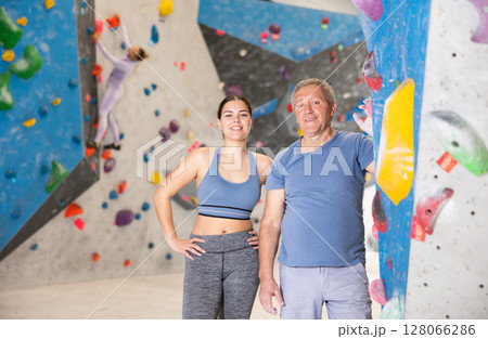 Sporty young girl and aged man standing near bouldering wall Sporty young girl and aged man standing near bouldering wall 128066286