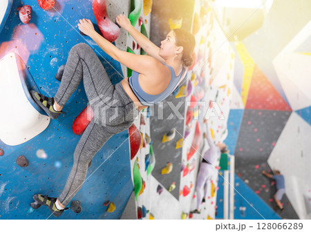 Young female alpinist practicing indoor rock-climbing on artificial boulder without safety belts 128066289