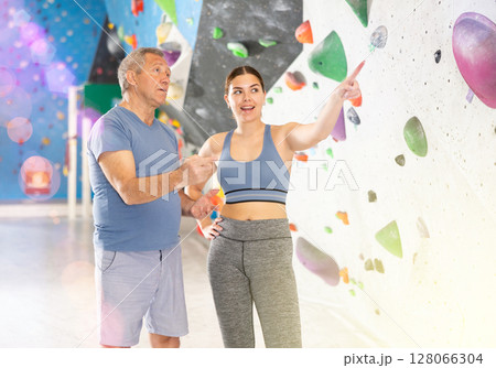 Trainer giving instructions to man on wall climbing at bouldering gym indoor 128066304