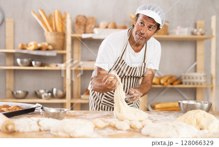 Adult male baker kneading dough on table 128066329