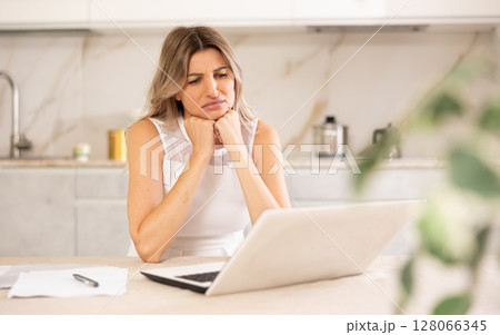 Disappointed woman sitting at table and looking at display of laptop 128066345