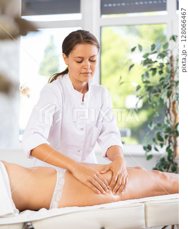 Young female massage therapist massaging front of woman thighs Young female massage therapist massaging front of woman thighs 128066467