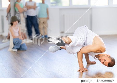 Experienced male trainer demonstrating to group of children dancers correct movements in hip-hop dance in choreography studio Experienced male trainer demonstrating to group of children dancers correct movements in hip-hop dance in choreography studio 128066607