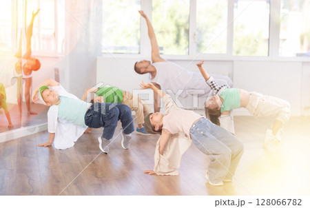 Dynamic young girl sitting in breakdance pose in dance studio with other teenage dancers 128066782