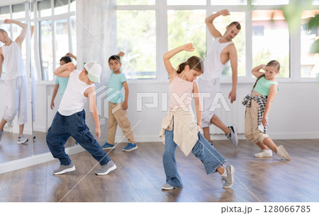Happy young girl and boy in casual clothes performing hip hop dance in dancing room during training with male teacher 128066785
