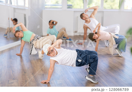 Dynamic happy boy training breakdance drops during workout session with group of children in studio 128066789