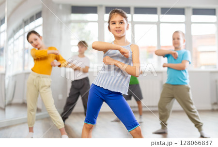 Positive juvenile girl engaged in breakdancing in training room with children's group 128066837