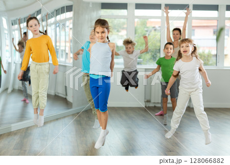 Group of positive juvenile boys and girls jumping cheerfully in dancehall Group of positive juvenile boys and girls jumping cheerfully in dancehall 128066882