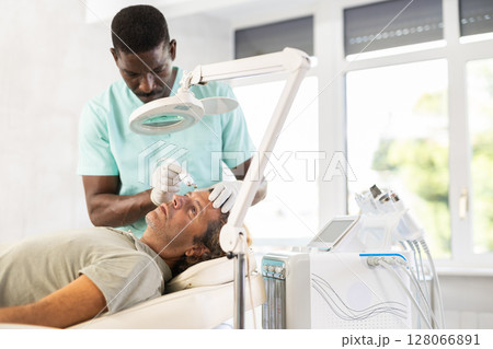 Adult male patient undergoing radiofrequency facial tightening procedure 128066891