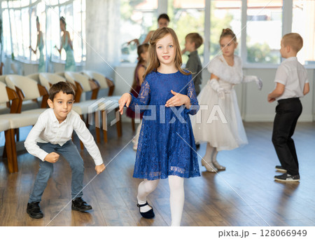 Little children in elegant dresses practicing twist dance in school hall Little children in elegant dresses practicing twist dance in school hall 128066949