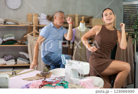 Elderly man and young woman doing warm-up exercises in sewing workshop Elderly man and young woman doing warm-up exercises in sewing workshop 128066980