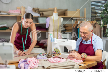 Senior man employee sewing, stitch clothes, girl apprentice draw dress pattern 128066999