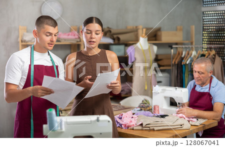 Female dressmaker with assistant reading documents in front of tailor 128067041