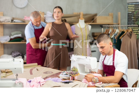 Mature man tailor takes measurements from girl client, guy work with sewing machine 128067047