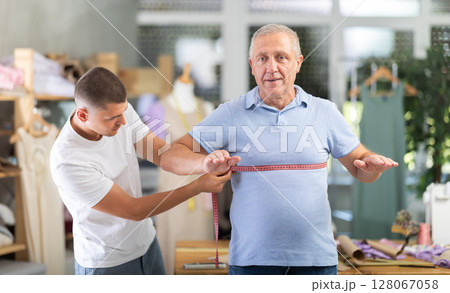 Young man tailor takes body measurements from elderly man 128067058