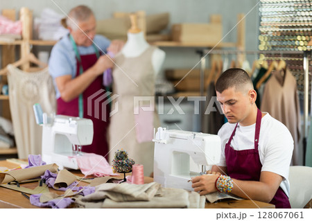 Young guy sews on machine male assistant sews on mannequin Young guy sews on machine male assistant sews on mannequin 128067061
