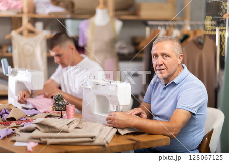 Elderly and young man sew on machine in workshop 128067125
