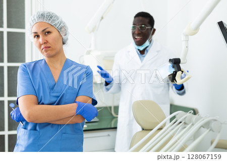 Frustrated female dental assistant standing in office with disgruntled doctor 128067159