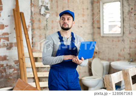 Builder handyman checking plan of house renovation on laptop Builder handyman checking plan of house renovation on laptop 128067163