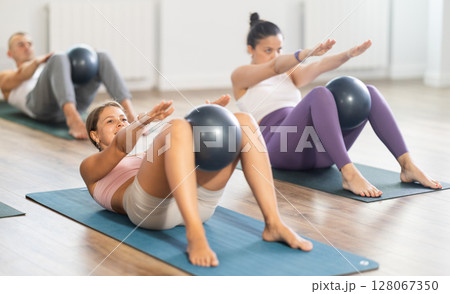 Young female Pilates instructor performing sit-ups with ball with group Young female Pilates instructor performing sit-ups with ball with group 128067350