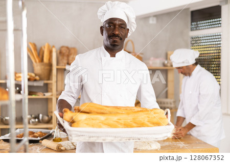 Successful African baker presenting golden baguettes in bakery Successful African baker presenting golden baguettes in bakery 128067352
