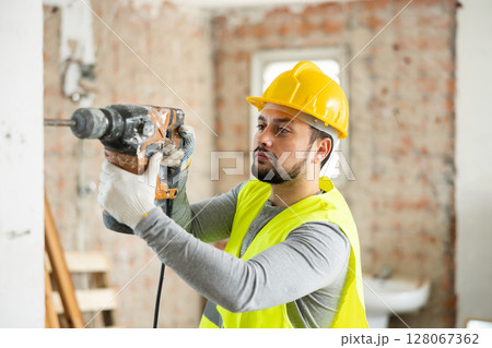 Professional builder drilling hole in wall with perforator in repairable room Professional builder drilling hole in wall with perforator in repairable room 128067362