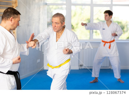Senior man in kimono honing punching techniques during training sparring Senior man in kimono honing punching techniques during training sparring 128067374