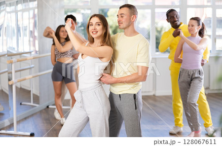 Happy young man and girl with group of international dancers training active swing in dance class Happy young man and girl with group of international dancers training active swing in dance class 128067611