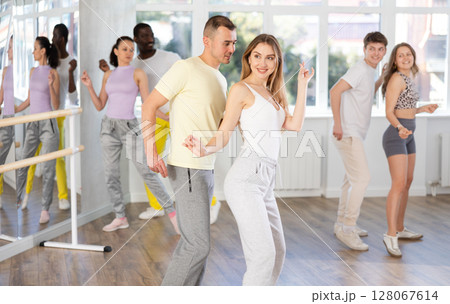 Group of young active multinational people dancing twist or rock and roll dance in dance hall during class 128067614