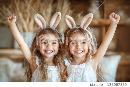 Two little girls with rabbit ears on light background, raised hands greeting, Easter concept. Two little girls with rabbit ears on light background, raised hands greeting, Easter concept. 128067889
