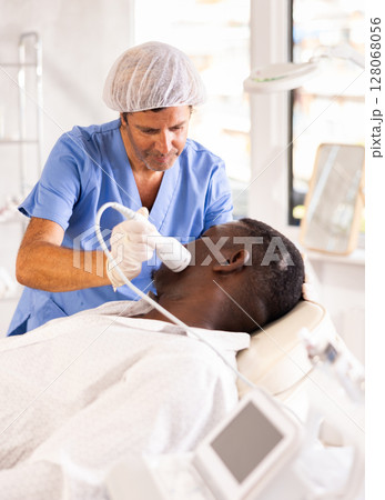 Cosmetologist performing facial cryotherapy procedure on african american Cosmetologist performing facial cryotherapy procedure on african american 128068056