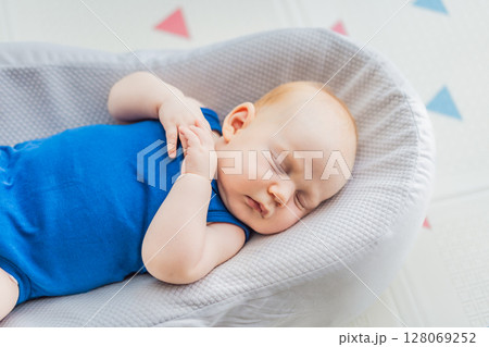 Chubby 3-month-old baby peacefully sleeping in a cozy baby nest at home. Concept of infant comfort, safety, and early development in a warm and nurturing environment 128069252