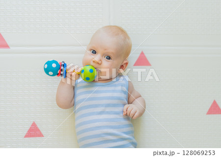 Adorable baby playing with colorful rattles on a soft baby play mat at home. Concept of early development, sensory play, and safe learning environment for infants 128069253