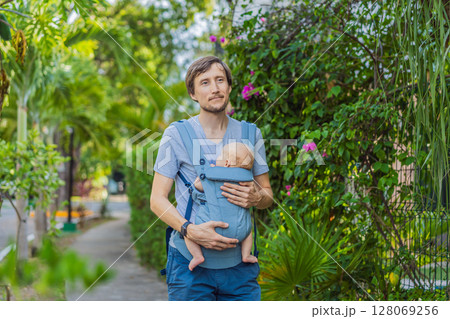 Young father walks in nature with his baby son nestled close in a parent-facing ergonomic baby carrier. Bonding, warmth, and modern parenting concept in a peaceful outdoor setting Young father walks in nature with his baby son nestled close in a parent-facing ergonomic baby carrier. Bonding, warmth, and modern parenting concept in a peaceful outdoor setting 128069256